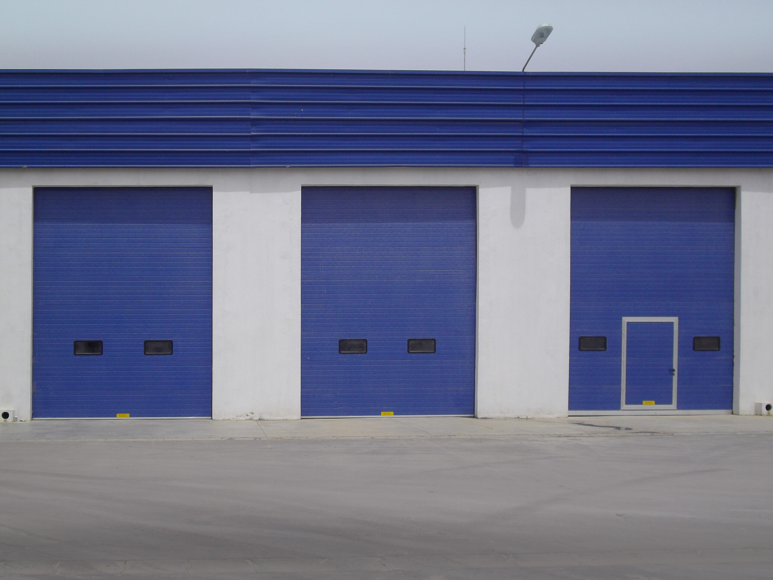 Portes sectionnelles industrielles avec hublots (une avec portillon intégré) couleur bleu.