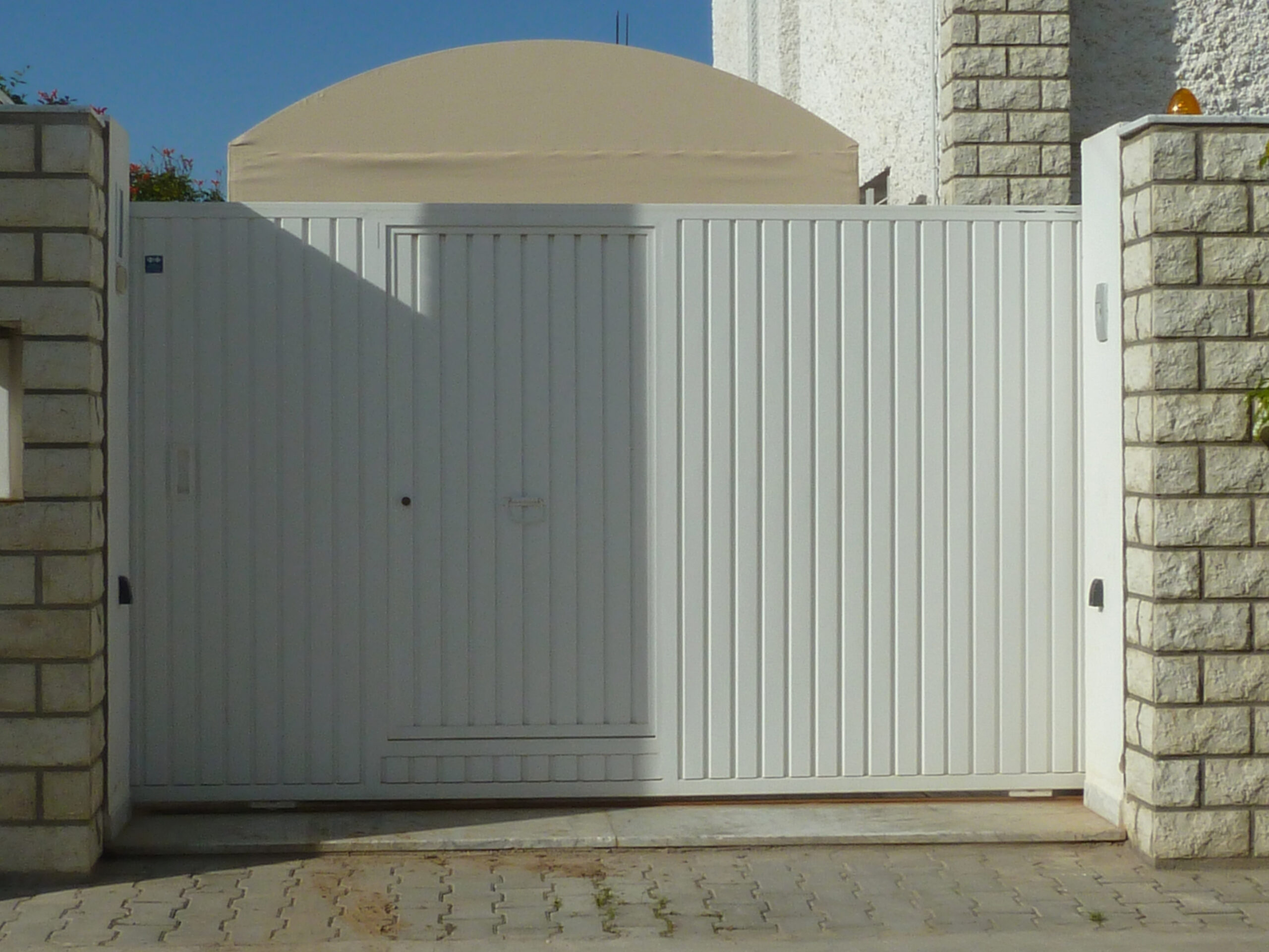 Porte coulissante motorisée en tôle nervurée simple paroi avec portillon intégré. Porte coulissante motorisée en tôle nervurée simple paroi avec portillon intégré.