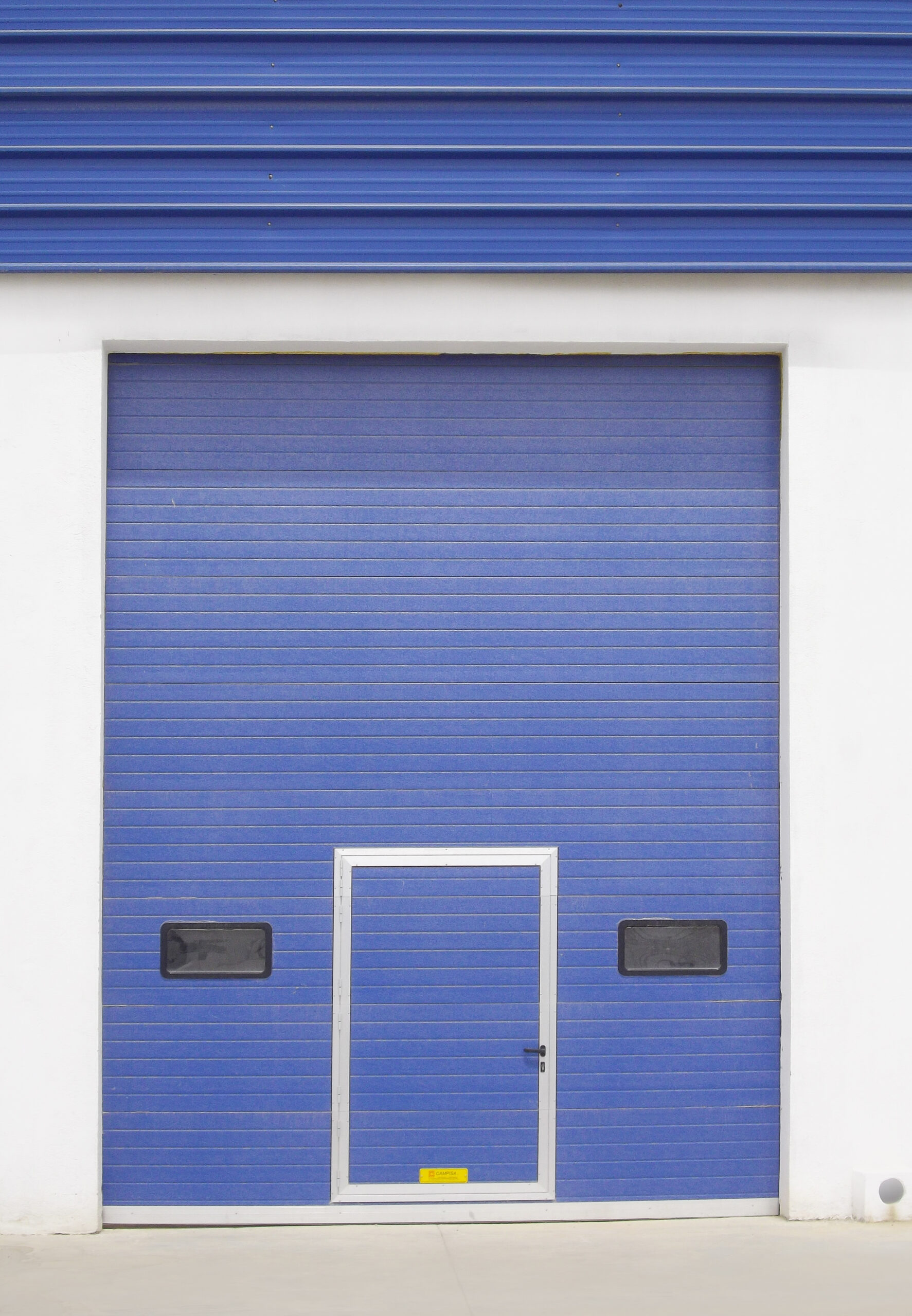 Portes sectionnelles industrielles avec hublots avec portillon intégré couleur bleu.