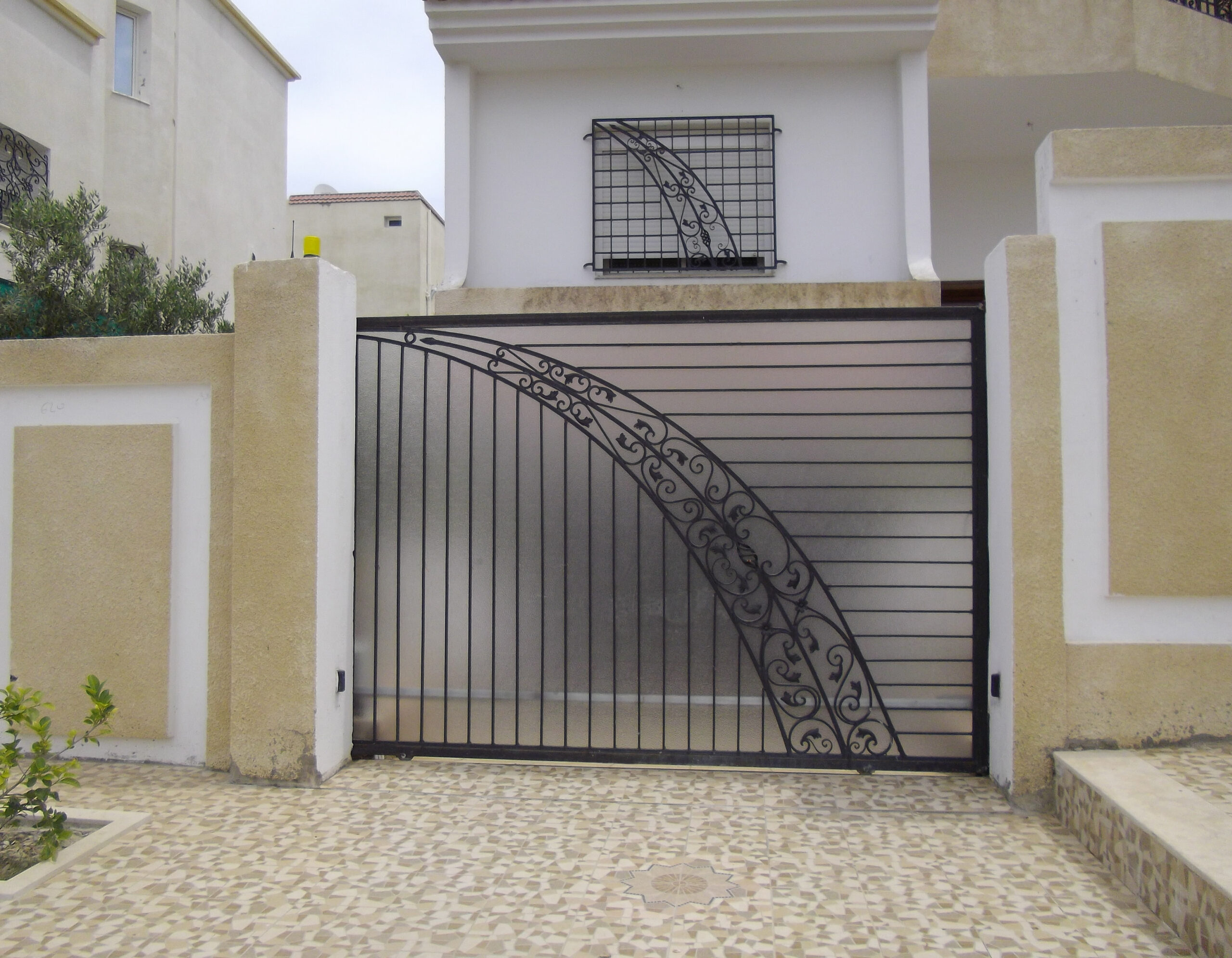 Porte coulissante motorisée en fer forgé motif arque, habillage en plexi. Porte coulissante motorisée en fer forgé motif arque, habillage en plexi.