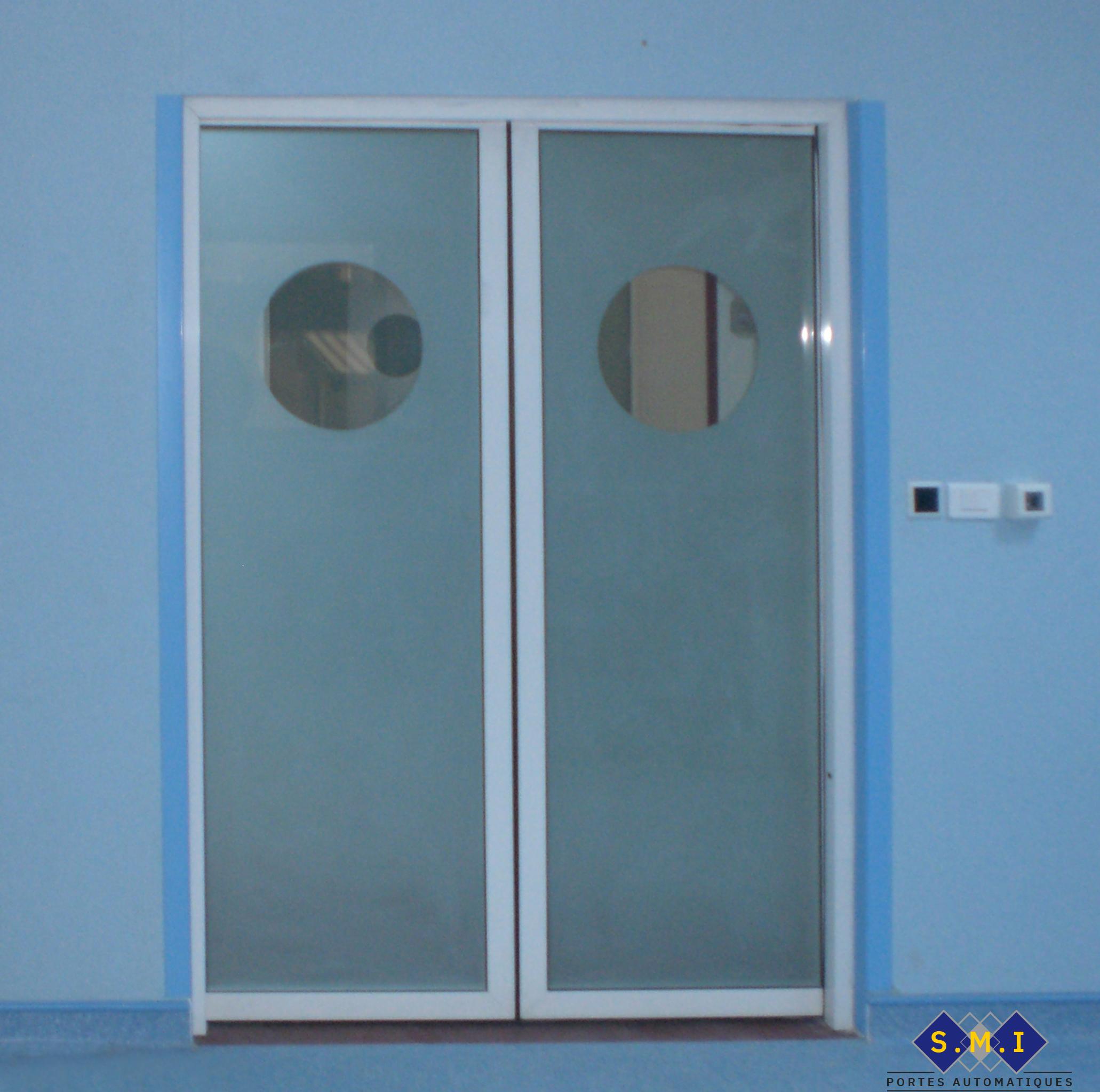 Porte radar à deux vantaux coulissants, verre sablé avec hublots claires commandée par sans touche pour salle opératoire. Porte radar à deux vantaux coulissants, verre sablé avec hublots claires commandée par sans touche pour salle opératoire.